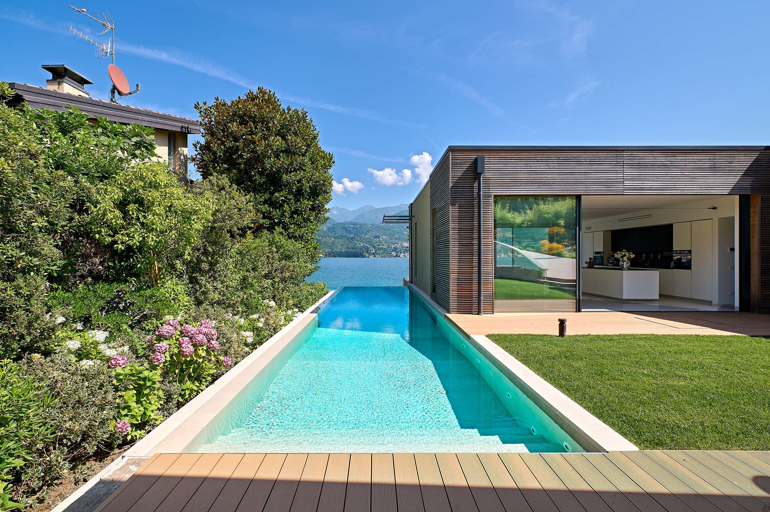 Piscina a sfioro verso il lago e il volume della casa con grandi vetrate scorrevoli